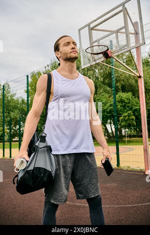 Ein entschlossener Mann in Sportbekleidung steht auf einem Basketballfeld und hält eine Tasche bereit für sein nächstes Training Stockfoto