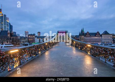 Fußgängerbrücke, eiserner Fußgängerbrücke mit Liebesschlössern am Geländer, Sonnenuntergang mit Blick auf die Skyline des Finanzviertels Frankfurt am Main Stockfoto