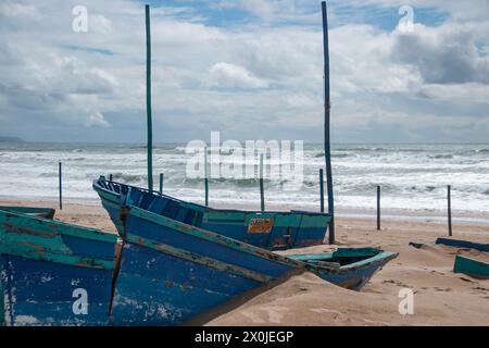 Hölzerne Boote sind am Strand gestrandet und fallen aufgrund des schlechten Wetters mit rauer See im Hintergrund Stockfoto