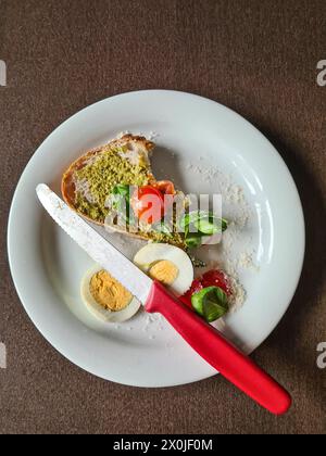 Ein Stück Brot mit Pesto-Aufstrich, Ei, Tomaten, Basilikum und Messer auf einem weißen Teller, Frühstück, Deutschland Stockfoto