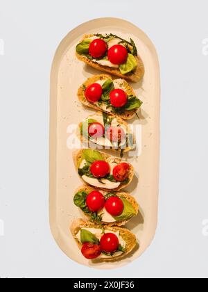 Servierplatte mit ganzen Cocktailtomaten und Mozzarella auf Brotscheiben mit Basilikum und Parmesan als Vorspeise Stockfoto