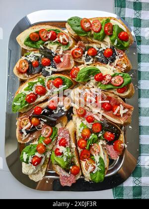 Servierplatte mit weißen Brotscheiben, Tomaten, Käse, Basilikum, Salami, bestreut mit Parmesan für eine italienische Note Stockfoto