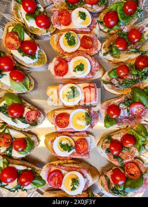 Brotscheiben mit Salami, in Scheiben geschnittenen Eiern, Tomaten, Mozzarella, Petersilie, basilikum-Blätter, grüner Pesto-Aufstrich Stockfoto