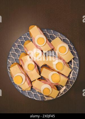 Hartgekochte Eier in Scheiben mit Käse und Schinken, serviert auf Brotscheiben auf einem Teller Stockfoto