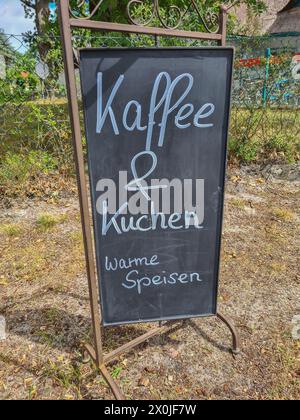 Ein Werbeschild für Kaffee, Kuchen und warme Speisen, handgeschrieben in Kreide, steht draußen im Sonnenlicht Stockfoto