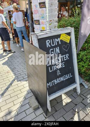 Ein handgeschriebenes Werbeschild steht vor dem Geschäft, das Rum, Gin, Souvenirs und Liköre von Zingst, Touristen im Hintergrund, Ostseebad Zingst, Deutschland, anbietet Stockfoto