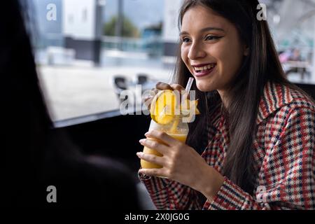 Eine junge lateinamerikanische Frau, die sich während eines Gesprächs einen Obstdrink teilt. Gesunde Lebenskonzepte Stockfoto