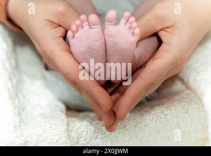 Mutterhände, die die Füße des Neugeborenen in Herzform halten Stockfoto