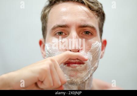 Gutaussehender kaukasier, der vorgibt, einen Schnurrbart mit dem Finger vor dem Spiegel zu haben. Movember-Konzept. Stockfoto