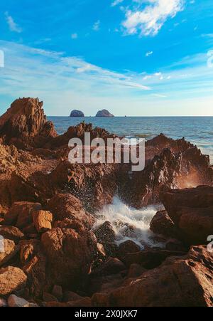 Eine mächtige Welle stürzt gegen die Rocky Shoreline und erschafft eine energiegeladene und dynamische Szene, die die rohe Kraft und Schönheit des Ozeans einfängt Stockfoto