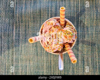 Ein farbenfroher Eisbecher mit drei Schaufeln Erdbeereis und bunten Streuseln, garniert mit drei gestreiften Eiskegeln, Mallorca, Spanien Stockfoto