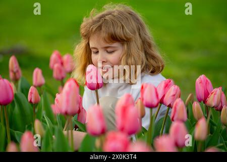 Spannfeder. Kinderspiel im Freien in einem schönen Frühlingsgarten. Kindergesicht in Tulpenblüten. Entzückendes kleines Kind im blühenden Tulpengarten auf der wunderschönen Stockfoto