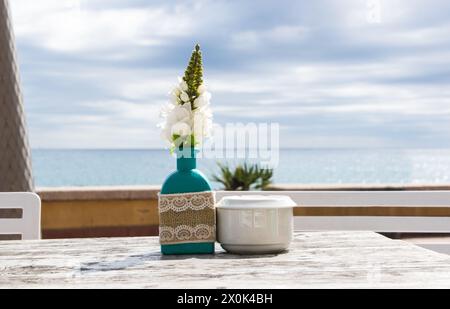 Lagerhaus im Freien. Stühle und Tische draußen bei Sommersonnenwetter. Vase mit Blumen auf dem Tisch für ein Sommercafé mit Meerblick. Stockfoto