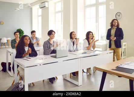 Eine Gruppe glücklicher Schüler sitzt an Schreibtischen im Klassenzimmer und klatscht mit den Händen Stockfoto