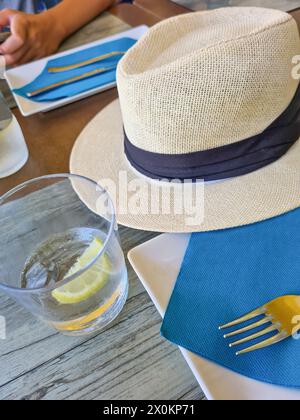 Ein Strohhut liegt im Schatten auf einem Tisch in den Sommerferien, verschwommener Hintergrund, Schwerpunkt liegt auf Strohhut als Sonnenschutz, Mallorca, Spanien Stockfoto