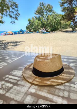 Ein Strohhut liegt im Schatten auf einem Tisch in den Sommerferien, verschwommener Hintergrund, Schwerpunkt liegt auf Strohhut als Sonnenschutz, Mallorca, Spanien Stockfoto