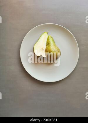Eine halbe Birne mit Stiel liegt mit beiden Hälften auf einer hellgrauen Platte, Thema gesunde natürliche Ernährung mit Früchten Stockfoto