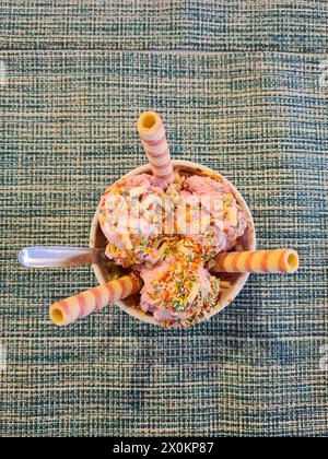 Ein farbenfroher Eisbecher mit drei Schaufeln Erdbeereis und bunten Streuseln, garniert mit drei gestreiften Eiskegeln, Mallorca, Spanien Stockfoto