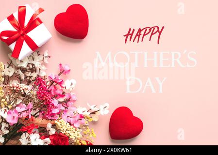 Alles Gute zum Muttertag. Blick von oben auf Blumen, Geschenkbox und rote Herzen mit dem Text Happy Mothers Day auf rosa Hintergrund Stockfoto