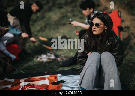 Junge Frau, die sich entspannt, während Freunde Hot Dogs auf einem Campingausflug kochen Stockfoto