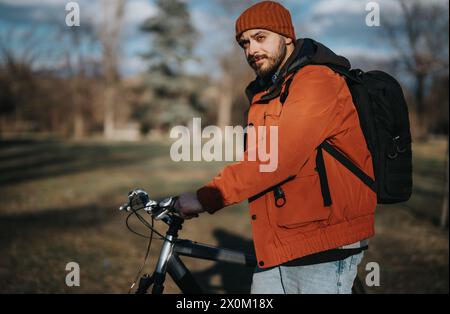 Stilvoller Mann mit Bart, der einen sonnigen Tag genießt, während er mit seinem Fahrrad im Park spaziert Stockfoto