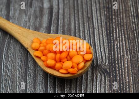 Rote Linsen in einem Holzlöffel auf einem alten Holztisch aus der Nähe. Vegetarische Gerichte. Stockfoto