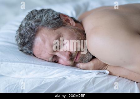 Ein Mann schläft im Bett. Blick von oben auf einen gutaussehenden Mann, der im Bett schläft. Gesunder Morgenschlaf. Der Typ schläft im Schlafzimmer. Erwachsene Männer mittleren Alters Stockfoto