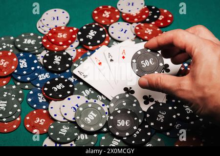 Vier Asse auf einem Haufen Spielchips auf dem grünen Tisch in der Nähe des Casinos. Konzentrieren Sie sich mit einem Chip in den Fingern auf die Hand des Spielers Stockfoto