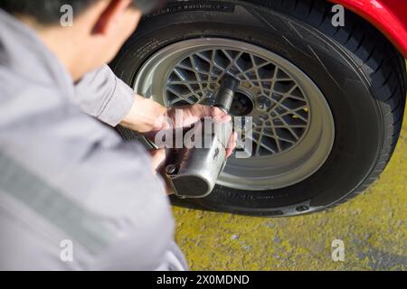 Ein Mechaniker in Uniform, der einen pneumatischen Schlagschrauber verwendet, um am Rad eines Autos zu arbeiten, wahrscheinlich während des Reifenwechsels oder der Durchführung von Wartungsanschlägen Stockfoto