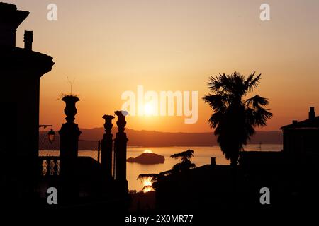Sonnenuntergang über dem See Bolsena mit Terrasse und Bäumen in der Silhouette von Montefiascone, Provinz Viterbo, Region Latium, Italien. April 2024 Stockfoto