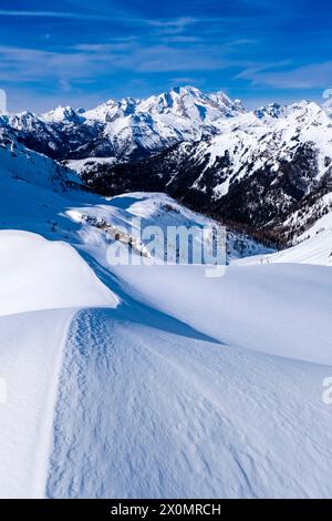 Schneetreiben schafft kunstvolle Strukturen rund um den Giau Pass im Winter, alpine Dolomitenlandschaft und schneebedeckte Gipfel der Marmolada Gruppe in der Ferne Stockfoto