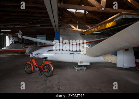 Flugplatz Ansbach Petersdorf, Deutschland. April 2024. Ein Moped steht vor mehreren überdachten Segelflugzeugen im Hangar eines Area Clubs. Quelle: Pia Bayer/dpa/Alamy Live News Stockfoto