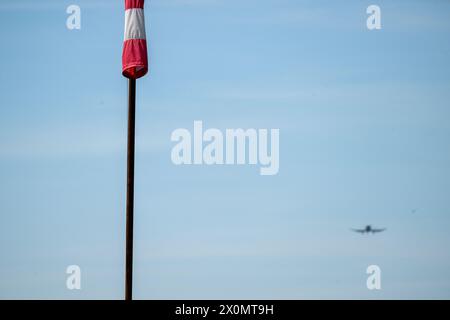 Flugplatz Ansbach Petersdorf, Deutschland. April 2024. Ein Flugzeug fliegt hinter einer locker hängenden Windfahne am blauen Himmel. Es bleibt sonnig. Quelle: Pia Bayer/dpa/Alamy Live News Stockfoto