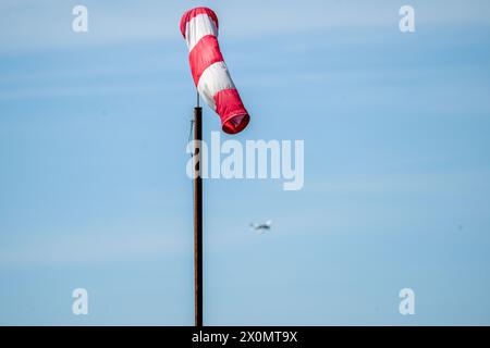 Flugplatz Ansbach Petersdorf, Deutschland. April 2024. Ein Flugzeug fliegt hinter einer locker hängenden Windfahne am blauen Himmel. Es bleibt sonnig. Quelle: Pia Bayer/dpa/Alamy Live News Stockfoto