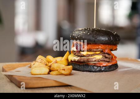 Köstlicher Black Beef Burger in Bun Bread mit Patty, Ketchup und Cheddar Käse auf Holzbrett. Fast Food Restaurant Stockfoto