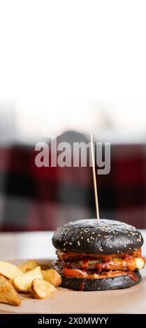 Frischer leckerer Burger in schwarzem Brötchen und Pommes Frites auf Holztisch. Unscharfer Hintergrund. Stockfoto