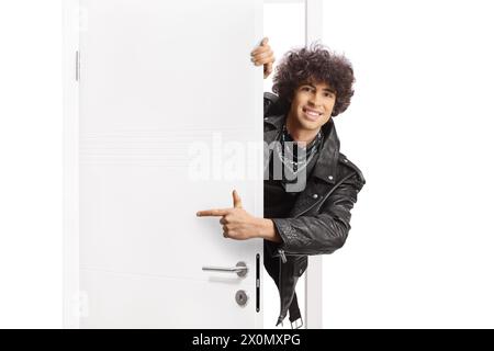 Junger Mann in einer schwarzen Lederjacke, der hinter einer Tür steht und zeigt Stockfoto