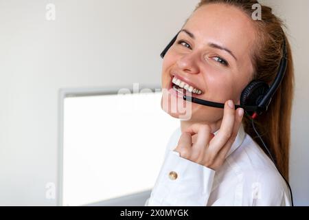 Glücklicher Mitarbeiter im Büro. Kundendienstmitarbeiterin im Headset, die auf die Kamera blickt und lächelt. Stockfoto