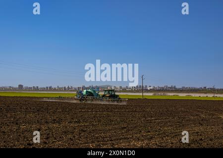 Landwirt mit Traktor bewirtschaftet Land in der Nähe der Großstadt an einem sonnigen Tag Stockfoto