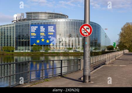 Europawahl 2024 Symbolbild für die europäische Verkehrspolitik das Schild für ein Verbot für Autos und Motorräder bzw. Alle Kraftfahrzeuge. Am dahinterliegenden EU-Parlament hängt Plakat zur Stimmabgabe bei den bevorstehenden Europawahlen 2024. Straßburg Robertsau Sud Ouest Bas-Rhin Frankreich *** Europawahlen 2024 symbolisches Bild für die europäische Verkehrspolitik das Zeichen für ein Verbot von Pkw und Motorrädern oder allen Kraftfahrzeugen im EU-Parlament dahinter hängt ein Poster zur Abstimmung bei den bevorstehenden Europawahlen 2024 Strasbourg Robertsau Sud Ouest BAS Rhin France 20240410-6V2A0487 Stockfoto