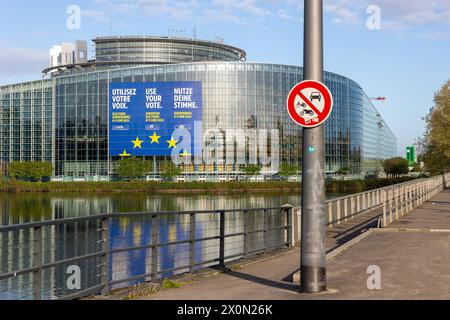 Europawahl 2024 Symbolbild für die europäische Verkehrspolitik das Schild für ein Verbot für Autos und Motorräder bzw. Alle Kraftfahrzeuge. Am dahinterliegenden EU-Parlament hängt Plakat zur Stimmabgabe bei den bevorstehenden Europawahlen 2024. Straßburg Robertsau Sud Ouest Bas-Rhin Frankreich *** Europawahlen 2024 symbolisches Bild für die europäische Verkehrspolitik das Zeichen für ein Verbot von Pkw und Motorrädern oder allen Kraftfahrzeugen im EU-Parlament dahinter hängt ein Poster zur Abstimmung bei den bevorstehenden Europawahlen 2024 Strasbourg Robertsau Sud Ouest BAS Rhin France 20240410-6V2A0486 Stockfoto