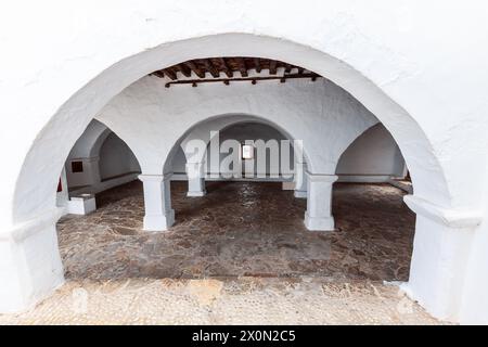 Im Inneren des Puig de Missa zeigt ein überdachter Innenhof eine ruhige Reihe von weißen Bögen und Säulen, die zu einem zentralen, gerahmten Eingang in Santa Eulalia führen. Stockfoto