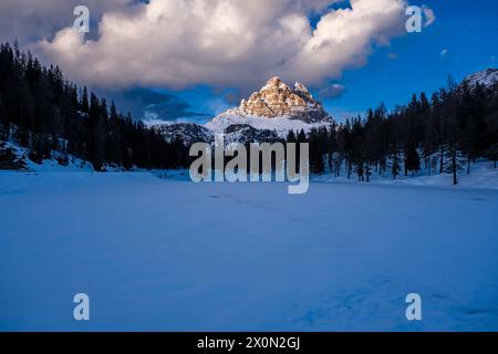 Der gefrorene und schneebedeckte See Lago d'Antorno, die alpine Dolomitenlandschaft und die Gipfel des Tre Cime di Lavaredo in der Ferne bei Sonnenuntergang. Stockfoto