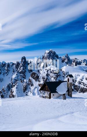 Die Kapelle Cappella degli Alpini im Naturpark Tre Cime im Winter, die alpine Dolomitenlandschaft und die Gipfel von Cadini di Misurina in der Ferne. Stockfoto