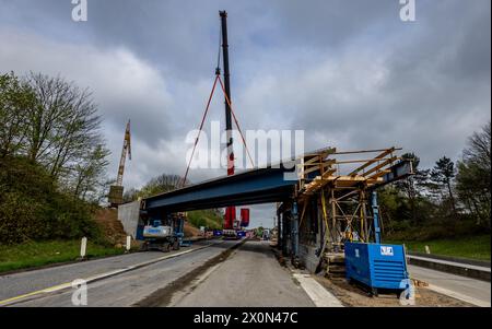 Owschlag, Deutschland. April 2024. Auf einer Baustelle an der Autobahn A7 zwischen den Anschlussstellen Owschlag und Rendsburg/Büdelsdorf werden vorgefertigte Brückenbauteile in Position gebracht. Die Fahrbahn in Richtung Hamburg wird vom 12. April 2024 von 20 Uhr bis 15. April 2024 um 5 Uhr gesperrt. Die Träger werden zunächst auf Tiefladern auf die Baustelle geliefert und dann mit einem 500-Tonnen-Kran in Position gebracht. Quelle: Axel Heimken/dpa/Alamy Live News Stockfoto