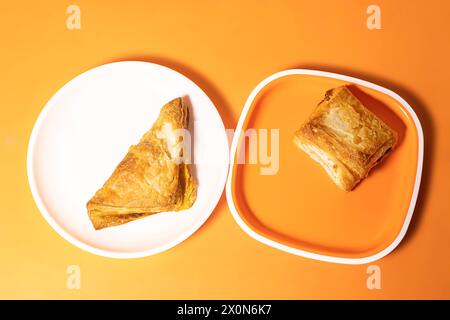 Zwei verschiedene Arten von knusprigen vegetarischen Blätterteigen auf einem Teller auf einem orangen Hintergrund. Draufsicht Stockfoto