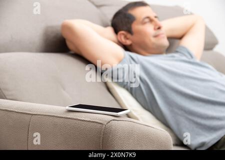 Nahaufnahme des Handys mit einem Mann, der müde ist und zu Hause auf dem Sofa schläft Stockfoto