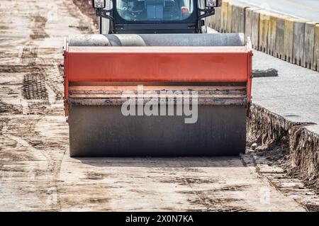 Die gelbe Straßenwalze mit geschlossener, klimatisierter Kabine steht auf einer noch nicht fertig gefertigten neuen Straße in Stonesat City Stockfoto