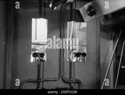 ENTWÄSSERUNG DES ROYAL NAVY-ZUGES AUF DEM MODERNEN SCHULSCHIFF. SEPTEMBER 1941 AN BORD DES ZERSTÖRER-DEPOT-SCHIFFES HMS TYNE. DIE DESTROYERMEN SIND AUSGEBILDET IN GESCHÜTZE, TORPEDOFEUER, U-BOOT-ABWEHR, SEEMANNSCHAFT UND SIGNALGEBUNG. ES WERDEN SCHIFFSMODELLE VERWENDET UND DIE BELEUCHTUNG IST SO ANGEORDNET, DASS SIE DIE EFFEKTE VON SCHEINWERFERN, STERNMUSCHELN UND GESCHÜTZBLITZEN ERZEUGT. - Männer, die als Kontrollbeamte ausgebildet sind, beobachten den "Fall des Schusses" im Schützenraum Stockfoto