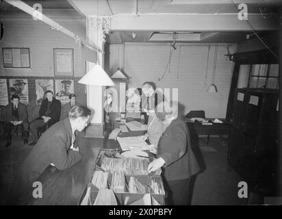 REGISTRIERUNG VON 16-JÄHRIGEN: JUGENDLICHE ERHALTEN IHRE AUSWEISKARTEN FÜR ERWACHSENE AN DER ARBEITSBÖRSE LONDON, ENGLAND, Großbritannien, 1945 - 16-jährige James Pickering (links) ist nicht gekommen, um sich für seinen Ausweiskarte für Erwachsene zu registrieren, wie die übrigen auf dem Foto sichtbaren Jugendlichen: er meldete sich freiwillig zur Handelsmarine und bat bei der Labour Exchange um die endgültige Erlaubnis, seinen jetzigen Job zu verlassen. Laut der Originalunterschrift hat er bereits einen Brief vorgelegt, der von seiner Mutter unterzeichnet wurde, der ihm erlaubt, sich anzuschließen, und hat einen Arzt bestanden. Die weiblichen Beamten des Arbeitsministeriums überprüfen seine Stockfoto